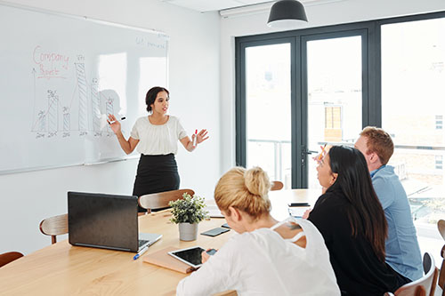 Indian young businesswoman standing near the whiteboard and explaining to business team new strategy of business during business presentation at office