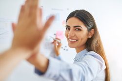 Gorgeous Indian woman in blue shirt high fiving coworkers at white board for concept about business development